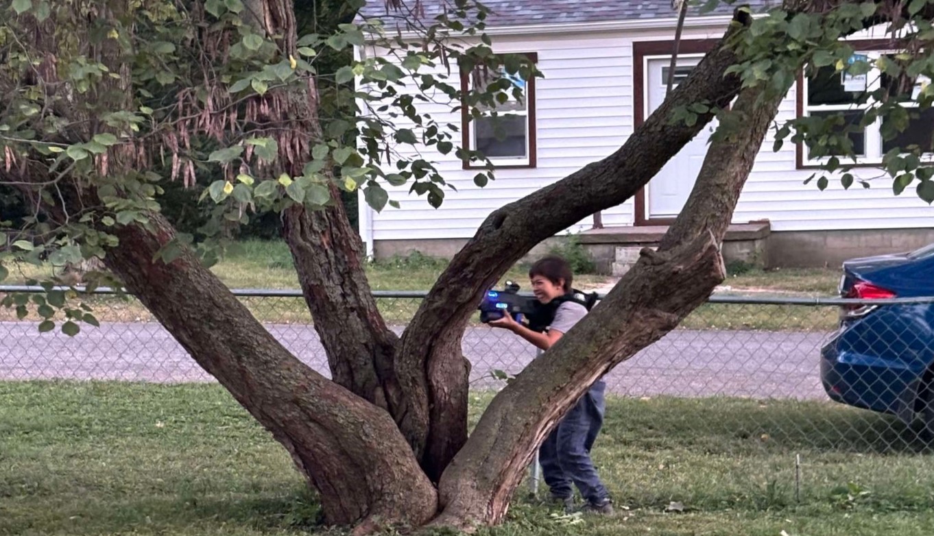 A kid hiding behind a tree while playing laser tag